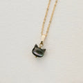 A gold chain necklace with a small cat-shaped pendant made of dark, iridescent mother-of-pearl, displayed on a textured white surface.